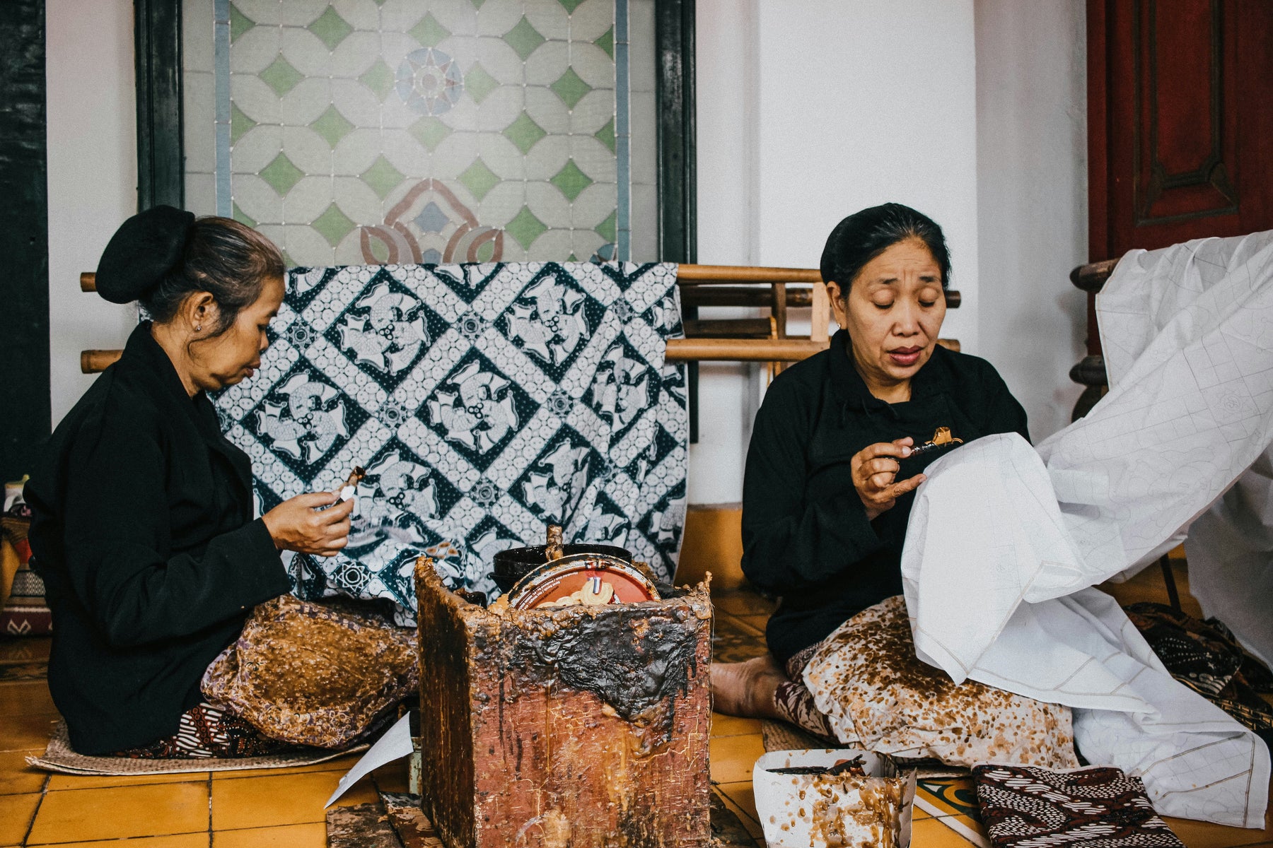 two seated women applying wax to batik fabric